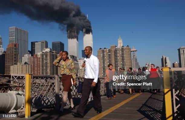 People walk over the Brooklyn Bridge as the world trade center burns September 11, 2001 after two hijacked airplanes slammed into the twin towers in...