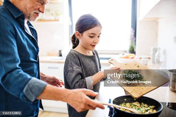 senior grandfather and granddaughter preparing food indoors in kitchen. - family small kitchen stock pictures, royalty-free photos & images