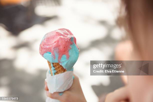 pink and blue ice cream melting in a cone and held by a child - girl eating messy ice cream cone stock-fotos und bilder