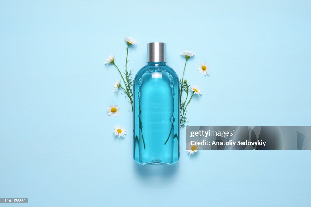 Botella cosmética y flores de manzanilla en la vista superior de la mesa azul