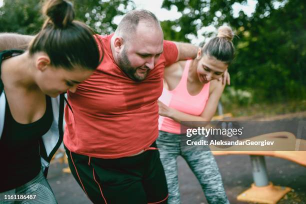 females helping overweight male walk after he got hurt in training - fat man lying down stock pictures, royalty-free photos & images