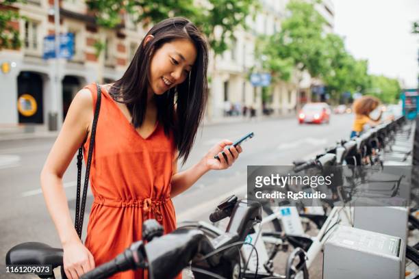 jonge vrouw die fiets neemt - bicycle rental stockfoto's en -beelden