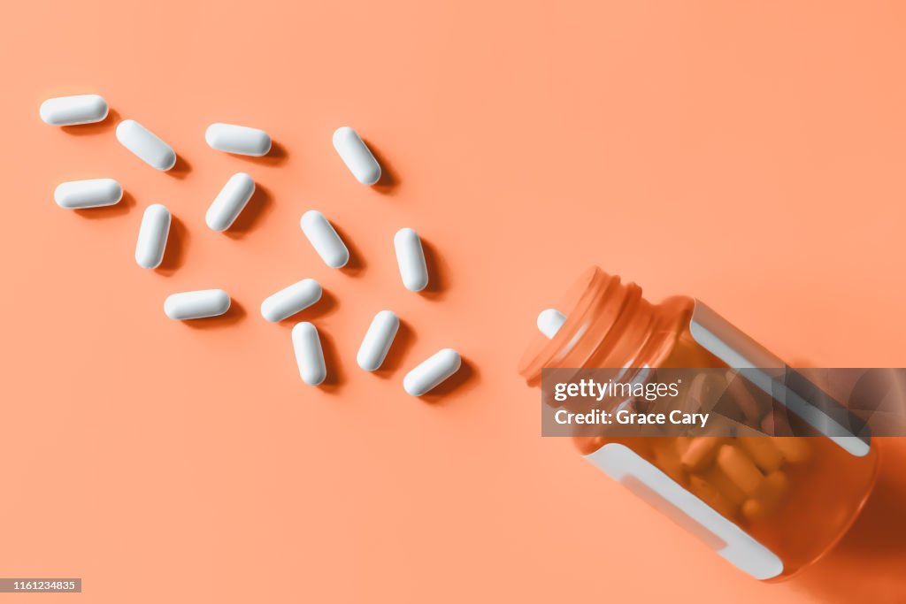 White pills spilling out of prescription bottle onto orange surface