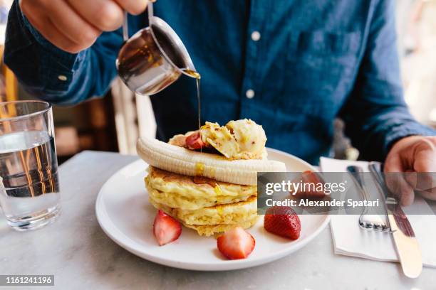 man pouring maple syrup on pancakes with banana and strawberry - eierkuchen speise stock-fotos und bilder