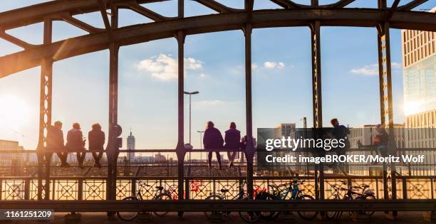 young people sitting on the balustrade of the hackerbruecke bridge over the railway tracks and looking into the distance, back light, munich, upper bavaria, bavaria, germany - munich 2018 stock pictures, royalty-free photos & images