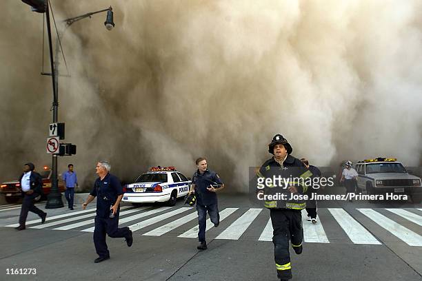 Policemen and firemen run away from the huge dust cloud caused as the World Trade Center's Tower One collapses after terrorists crashed two hijacked...