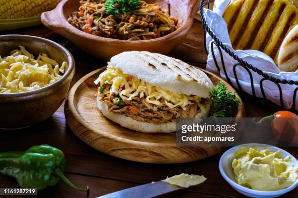 venezuelan traditional food, arepa with shredded cheese and meat (pelua). ingredients on a table in a rustic kitchen. - venezuela stock pictures, royalty-free photos & images