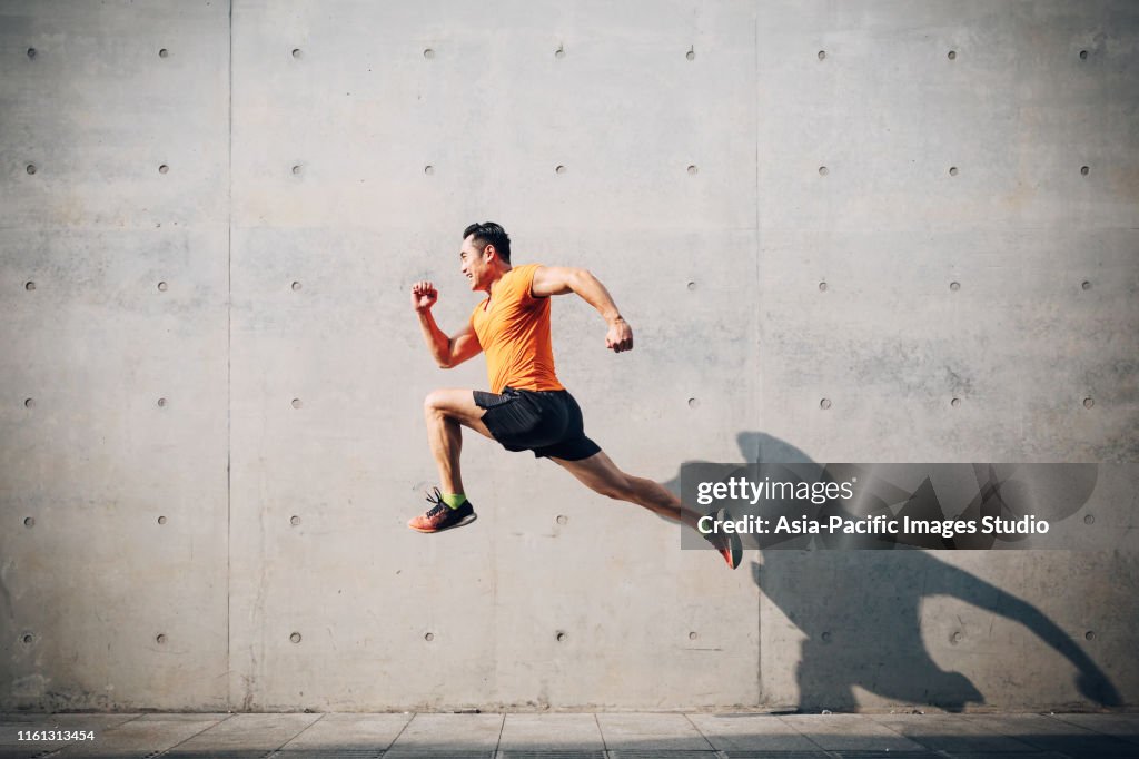 Sportlicher asiatischer Mittelsmann läuft und springt gegen Denkladen. Gesundheits- und Fitnesskonzept.