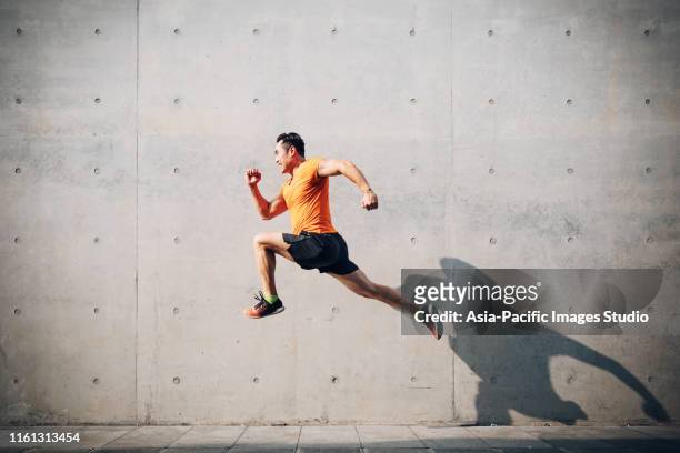 sporty asian mid man running and jumping against shutter. health and fitness concept. - mid adult stock pictures, royalty-free photos & images