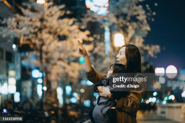 young asian mother embracing cute little daughter while enjoying the beautiful cherry blossom in the city at night - mother and daughter on night street stockfoto's en -beelden