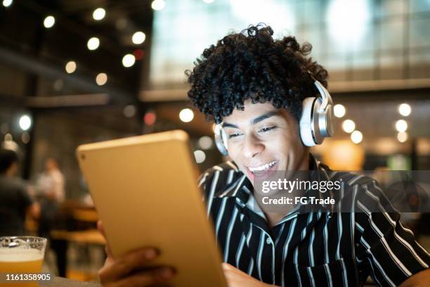 man using digital tablet and headphone in a restaurant - pardo brazilian stock pictures, royalty-free photos & images