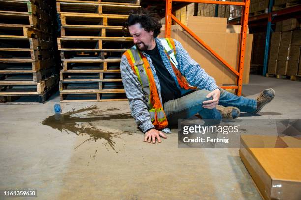 an industrial, warehouse, workplace safety topic.  an employee falls injuring himself by slipping on a plastic water bottle. - tropeçar imagens e fotografias de stock