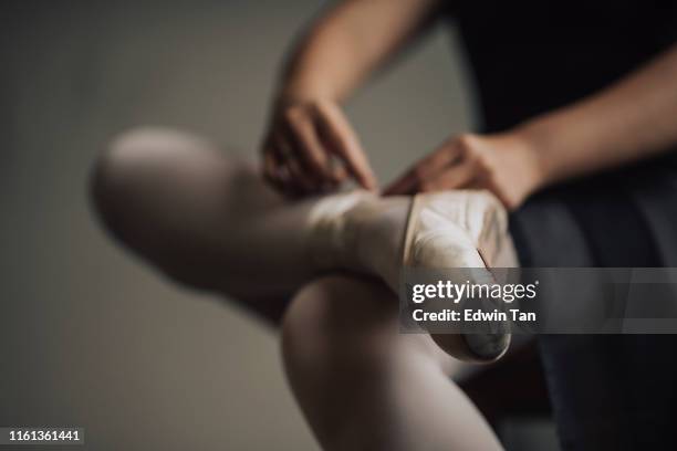 eine junge asiatische chinesische balletttänzerin, die sich darauf vorbereitet, ihren schnürsenkel zu binden, bevor sie ihren balletttanz im ballettstudio übt - ballettschuh stock-fotos und bilder
