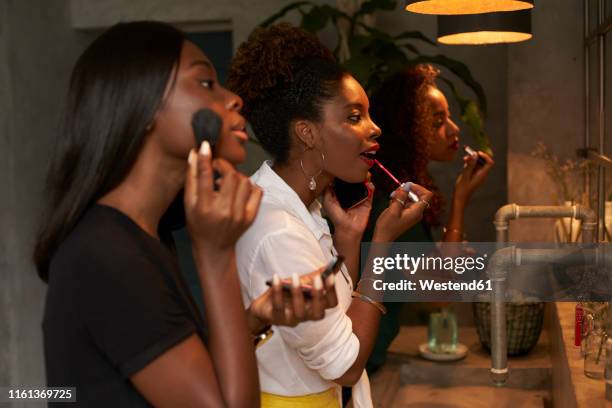 three friends applying makeup at ladies' room - girls night stock-fotos und bilder