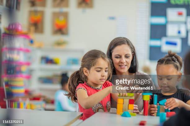 pre-school teacher playing with girls in kindergarten - preschool building fotografías e imágenes de stock