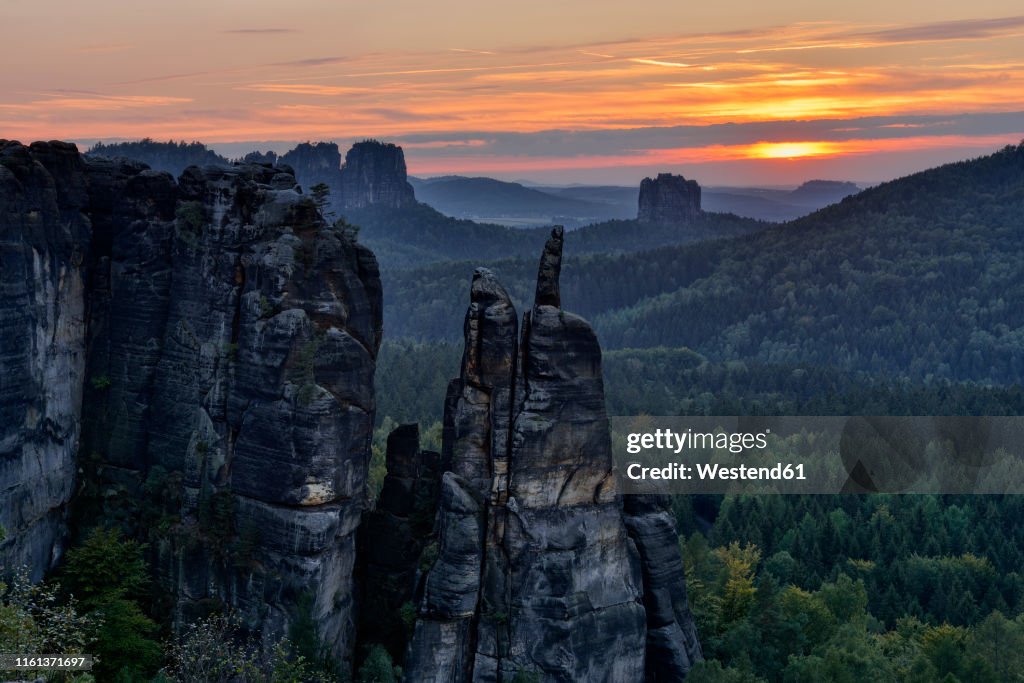 Germany, Saxony, Elbe Sandstone Mountains, sandstone rock Brosinnadel with Falkenstein and Schrammsteine in background at sunset