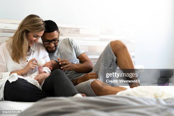 happy father and mother bottle-feeding their newborn baby in bed - parents and new born stock pictures, royalty-free photos & images