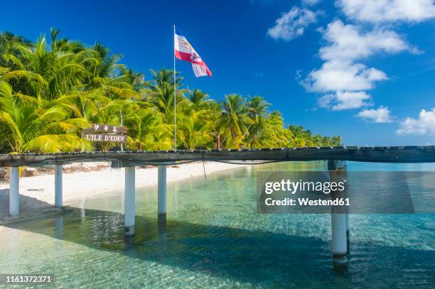 french polynesia, tuamotus, tikehau, pier at palm beach with flag - french polynesia stock pictures, royalty-free photos & images