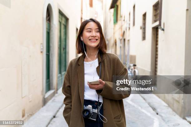 italy, florence, happy young woman with earphones and cell phone in an alley - florence italy city stock pictures, royalty-free photos & images