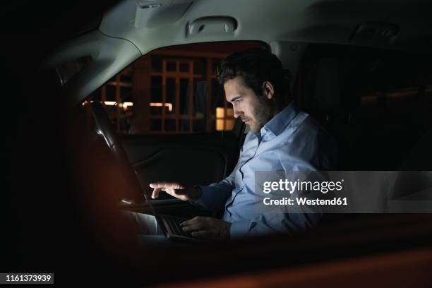 young man using laptop in car at night - inside car stockfoto's en -beelden