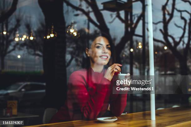 smiling young woman with cup of coffee behind windowpane in a cafe - coffee cup top view fotografías e imágenes de stock