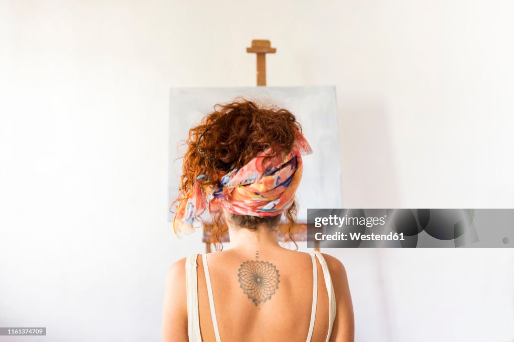 Rear view of young female painter in art studio in front of empty canvas