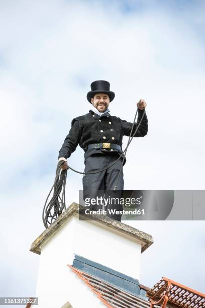 portrait of smiling chimney sweep working on house roof - rauchfangkehrer stock-fotos und bilder