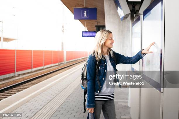 smiling woman checking the departures board at station platform - fahrplan stock-fotos und bilder