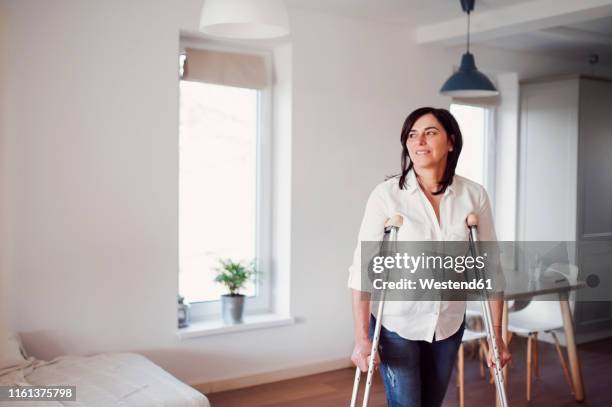 mature woman with crutches, alone at home - crutch stock-fotos und bilder