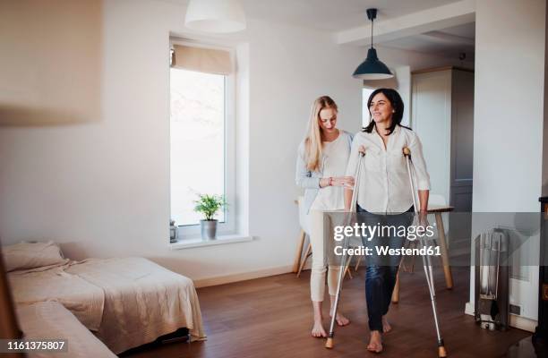 daughter helping her mother to walk with crutches - crutch bildbanksfoton och bilder