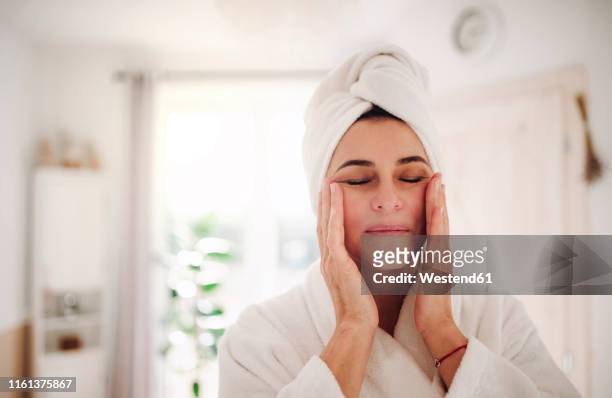 portrait of mature woman in a bathroom at home applying moisturizer - cream for face stock-fotos und bilder