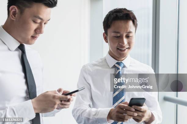 junge chinesische männliche führungskräfte überprüfen ihre smartphones - 2 men chatting casual office stock-fotos und bilder