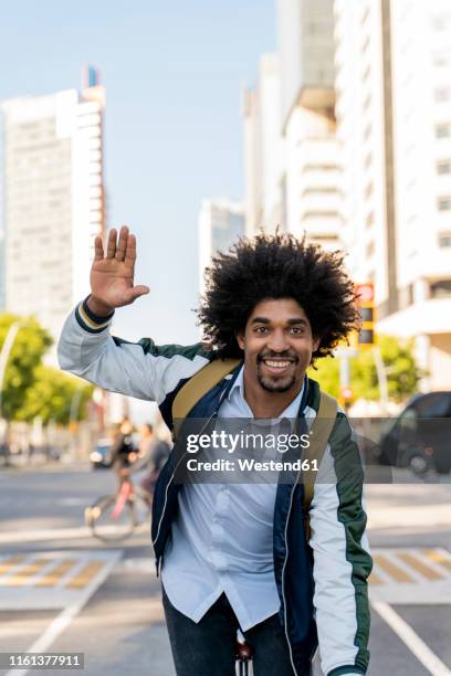 smiling casual businessman on bicycle in the city waving, barcelona, spain - curly waves stock pictures, royalty-free photos & images