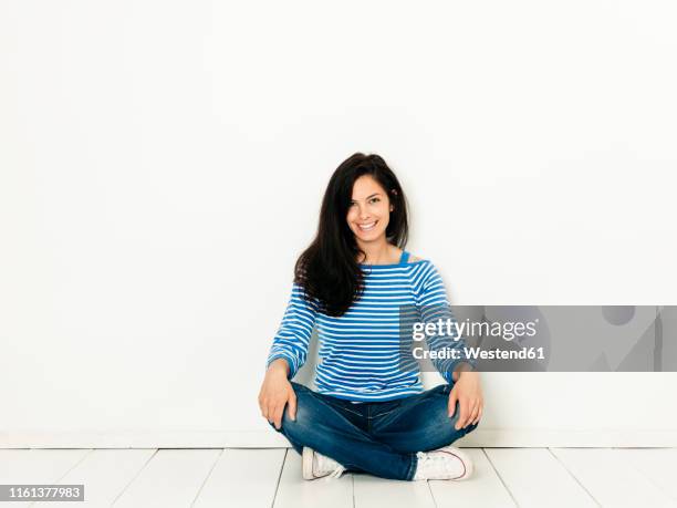 beautiful young woman with black hair and blue white striped sweater sitting on the ground in front of white background - sitting on ground stock pictures, royalty-free photos & images