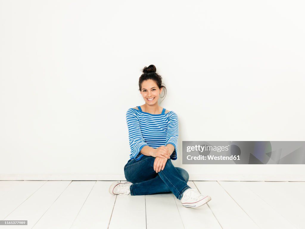 Beautiful young woman with black hair and blue white striped sweater sitting on the ground in front of white background