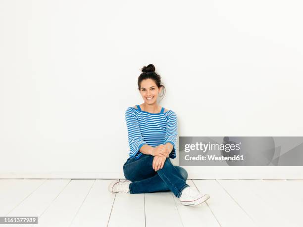 beautiful young woman with black hair and blue white striped sweater sitting on the ground in front of white background - sitting on floor fotografías e imágenes de stock