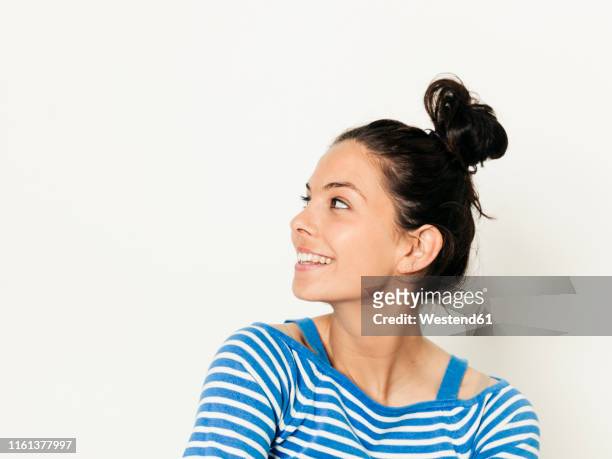 beautiful young woman with black hair and blue white striped sweater is posing in front of white background - mirada de reojo fotografías e imágenes de stock