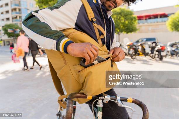 casual businessman with bicycle taking cell phone out of backpack in the city, barcelona, spain - taking off coat stock pictures, royalty-free photos & images