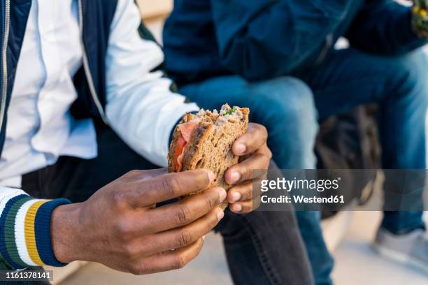 close-up of two men sitting on stairs having lunch break - sandwich stock-fotos und bilder