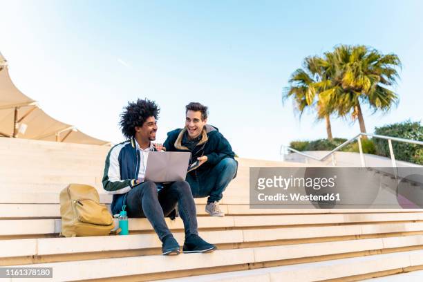 two happy casual businessmen sitting on stairs working on laptop - founder stock pictures, royalty-free photos & images