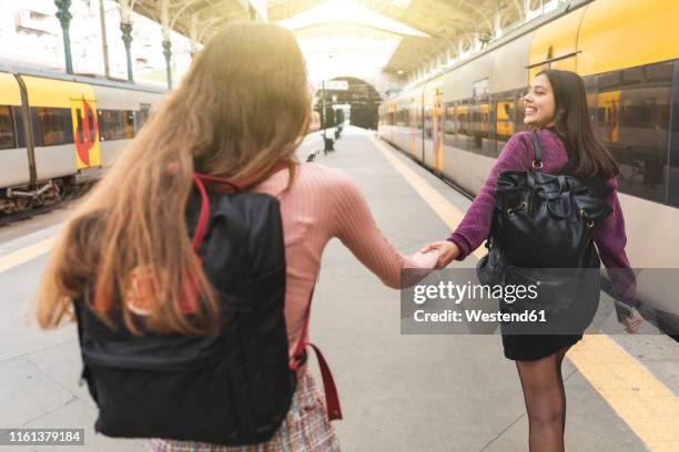 back view of two young women with backpacks hand in hand on platform, porto, portugal - woman pulling hair back stock pictures, royalty-free photos & images