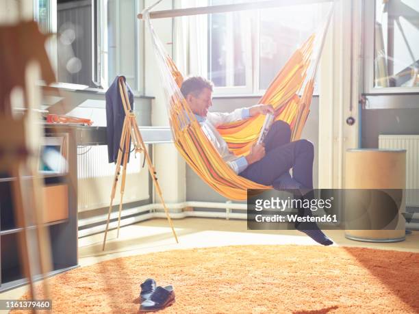 mature businessman reading magazine in hammock at office - escaping office stock pictures, royalty-free photos & images