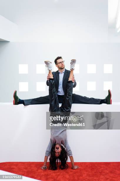businessman in office holding woman's legs doing a handstand - businesswoman handstand stock pictures, royalty-free photos & images