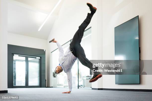 businessman with cell phone doing a one-handed handstand on office floor - acrobatic activity stock-fotos und bilder