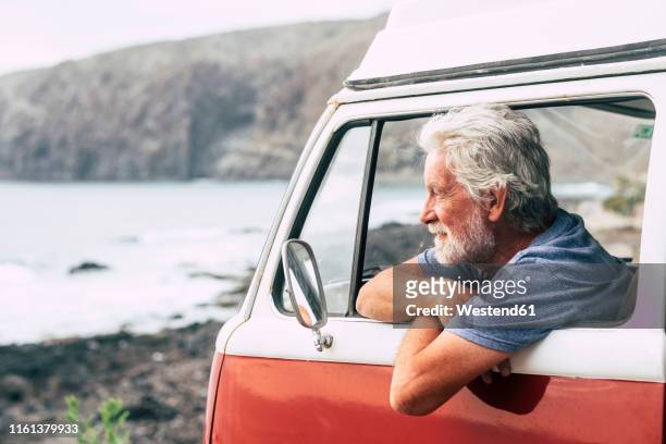 senior man travelling in a vinatge van, looking at the sea - auto alt stock-fotos und bilder