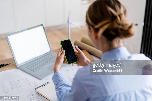 woman in office using cell phone with wind turbine model on table - femme de dos smartphone photos et images de collection