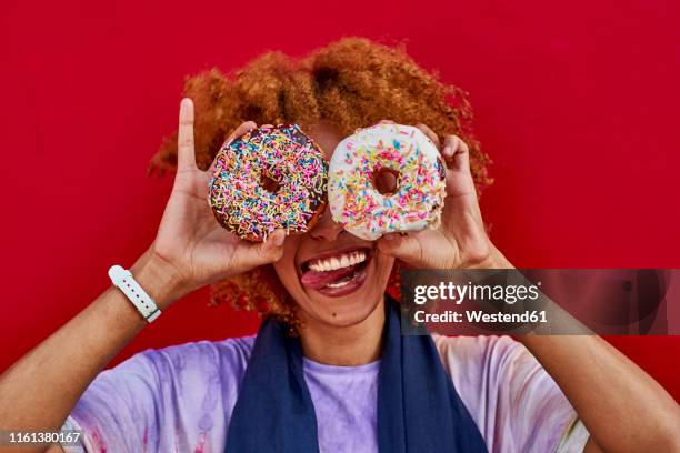 playful woman holding two donuts in front of her eyes - holding two things foto e immagini stock