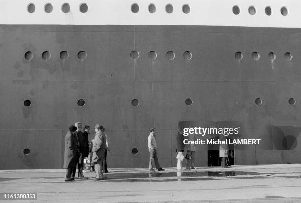 Des badauds regardent le paquebot 'Queen Elizabeth 2 ' dans le port de Cherbourg pendant la réparation de sa coque déchirée le 29 octobre 1974,...