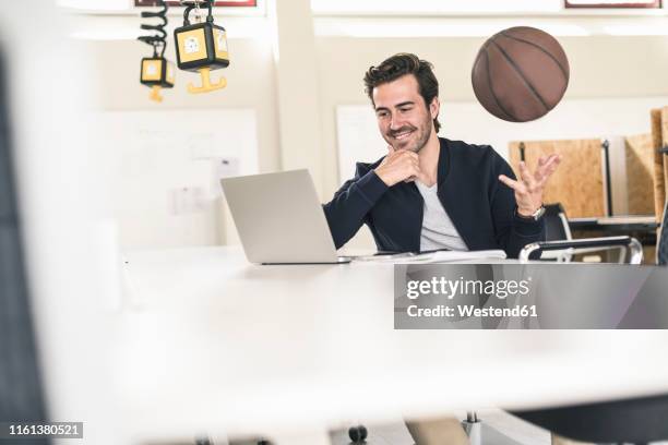 young businessman using laptop, playing with a basketball - basketball all access stock pictures, royalty-free photos & images