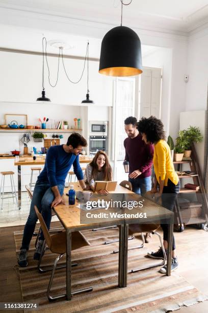 four friends in dining room at home with book - conference dining table stockfoto's en -beelden